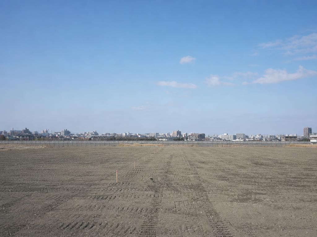 整地された広い開発用地と遠景の街並み、澄んだ青空
